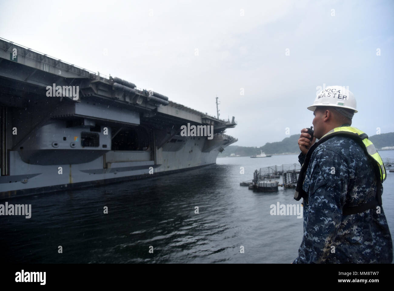 170908-N-JT445-034 YOKOSUKA, Japan (Sept. 8, 2017) Boatswain’s Mate 2nd Class Akran Omar from Fleet Activities (FLEACT) Yokosuka’s port operations, oversees the departure of USS Ronald Reagan (CVN 76), as the ship gets underway from FLEACT Yokosuka. Ronald Reagan is the flagship of Carrier Strike Group 5, providing a combat-ready force that protects and defends the collective maritime interests of its allies and partners in the Indo-Asia-Pacific region. FLEACT Yokosuka provides, maintains, and operates base facilities and services in support of 7th Fleet’s forward-deployed naval forces, 71 ten Stock Photo