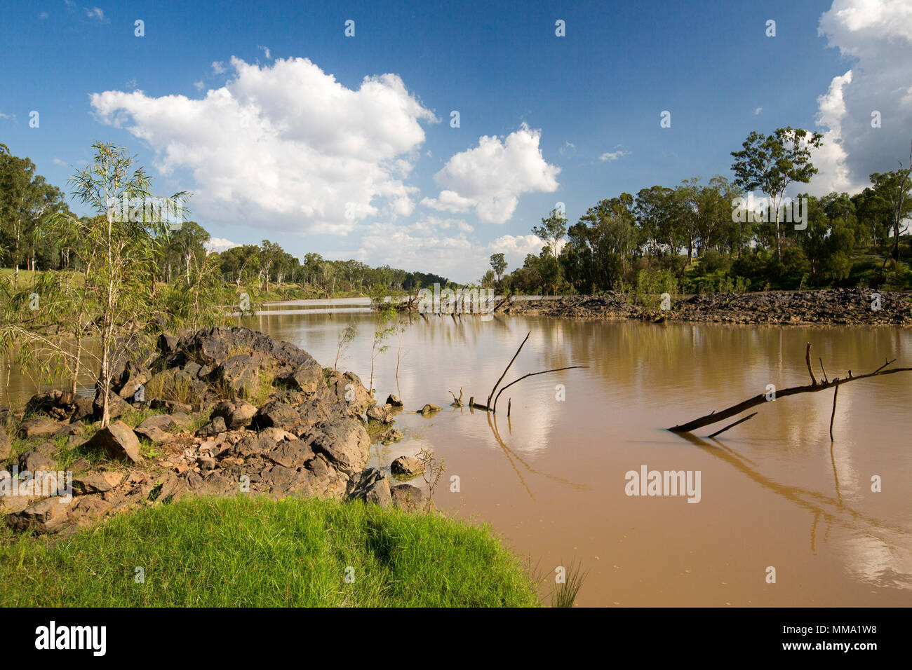 Colourful landscape with calm waters of Fitzroy River hemmed with tall trees and emerald grass under blue sky in central Queensland Australia Stock Photo