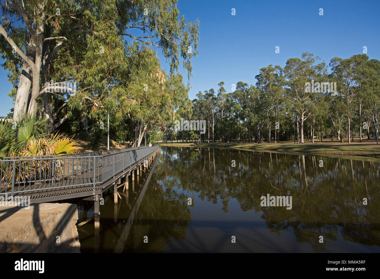 Picturesque landscape at Hood's Lagoon with surrounding trees of parklands & blue sky reflected in calm water at Clermont outback Queensland Australia Stock Photo