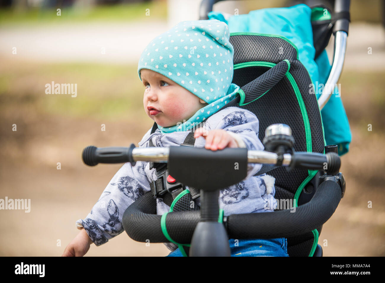 Cute baby girl in heat riding her tricycle in spring park Stock Photo