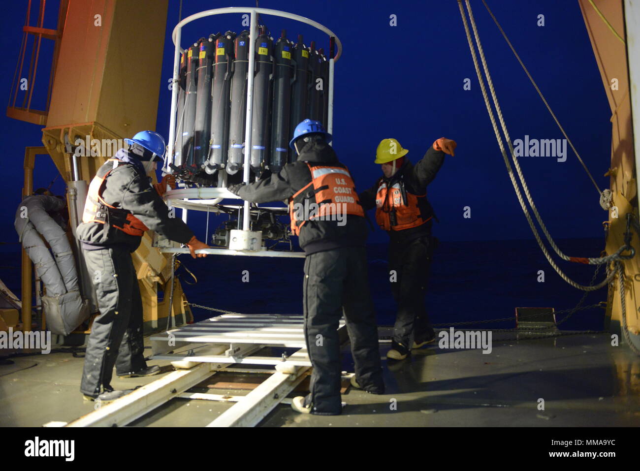 Coast Guard Seaman Frank Lenihan, Coast Guard Seaman Blake Berryman and Guard Chief Petty Officer William Winegar stabilize a water-sampling device, while Winegar also directs a machinery operator, as they lower the device onto the Coast Guard Cutter Healy during night operations along Barrow Canyon, Friday, Sept. 1, 2017.    The device was an oceanography instrument primarily used to determine the conductivity, temperature and depth of the ocean, as well as provide water samples form various depths for further analysis.     U.S. Coast Guard photo by Petty Officer 3rd Class Amanda Norcross Stock Photo