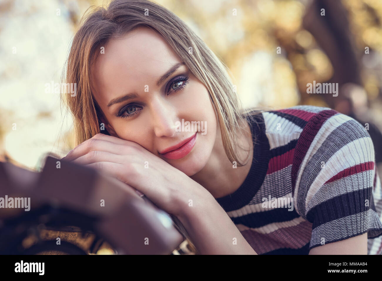 Close-up portrait of young blonde woman sitting on a bench in the ...