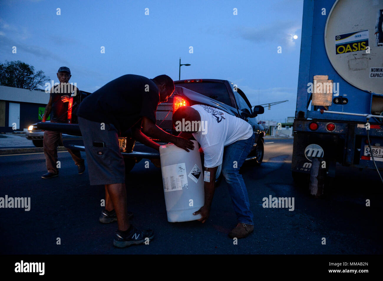 Elio Lopez Perez, right, a city employee working to give citizens drinking water, helps Jose Hernandez, middle, and Joe Peña lift their water container into their truck in San Juan, Puerto Rico, Oct. 3, 2017. The people of Puerto Rico are resilient, evidenced by the stories of neighbor helping neighbor, and communities helping communities after Hurricane Maria devastated the island. (U.S. Air Force photo by Master Sgt. Joshua L. DeMotts) Stock Photo