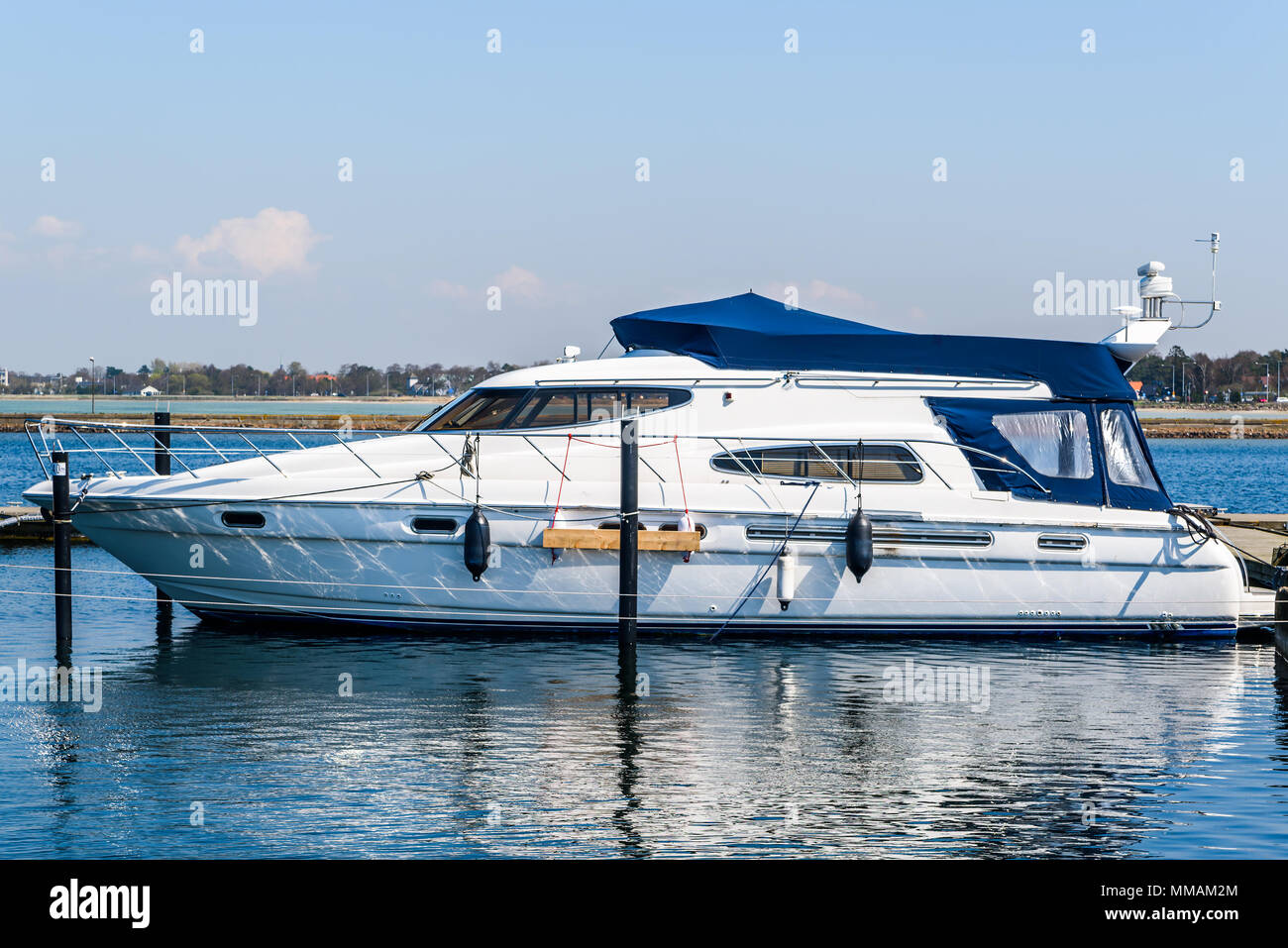 Luxurious white motorboat tied to a pier in a marina on a sunny warm day. Logos and id removed. Stock Photo