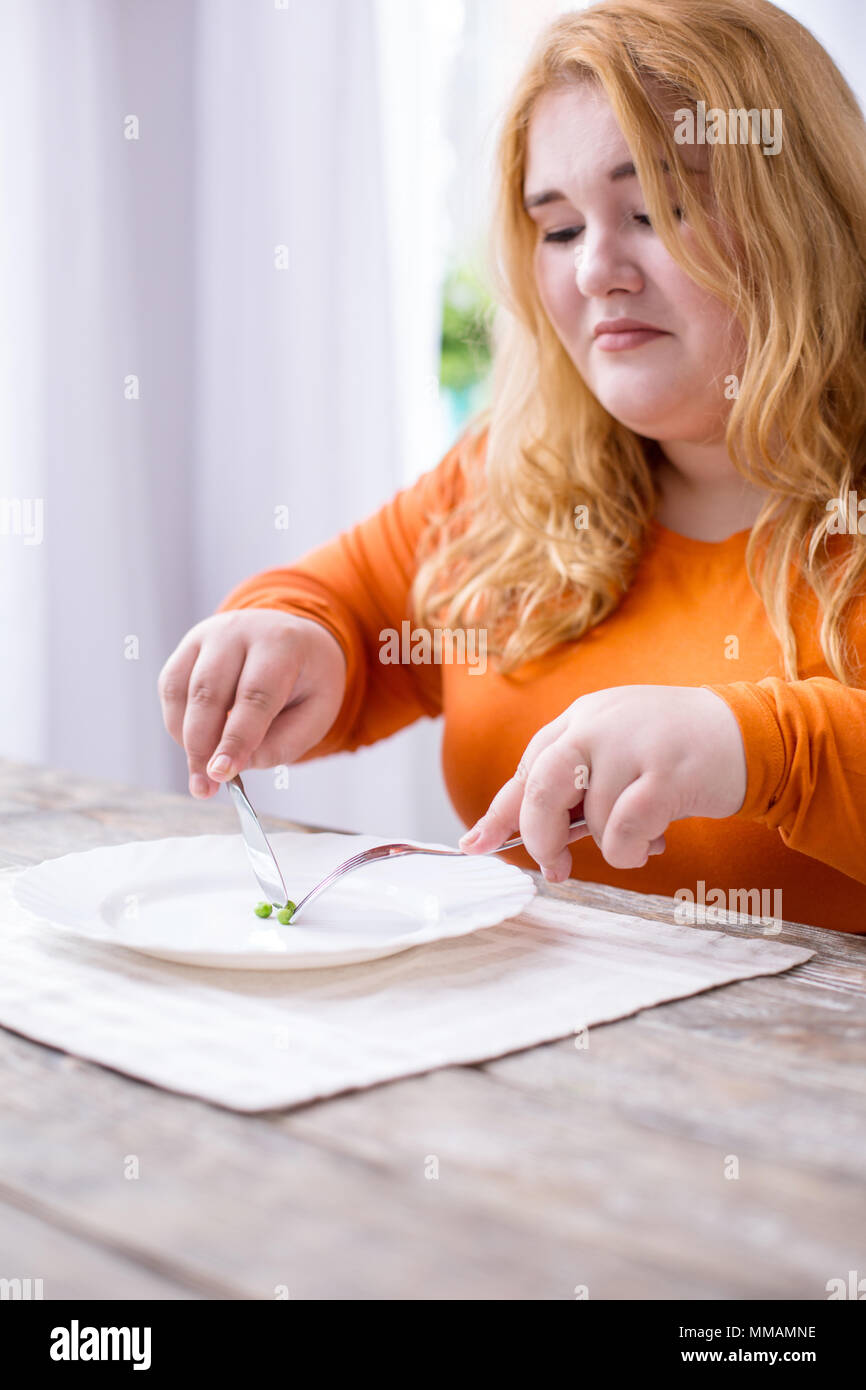 Dismal stout woman eating peas Stock Photo