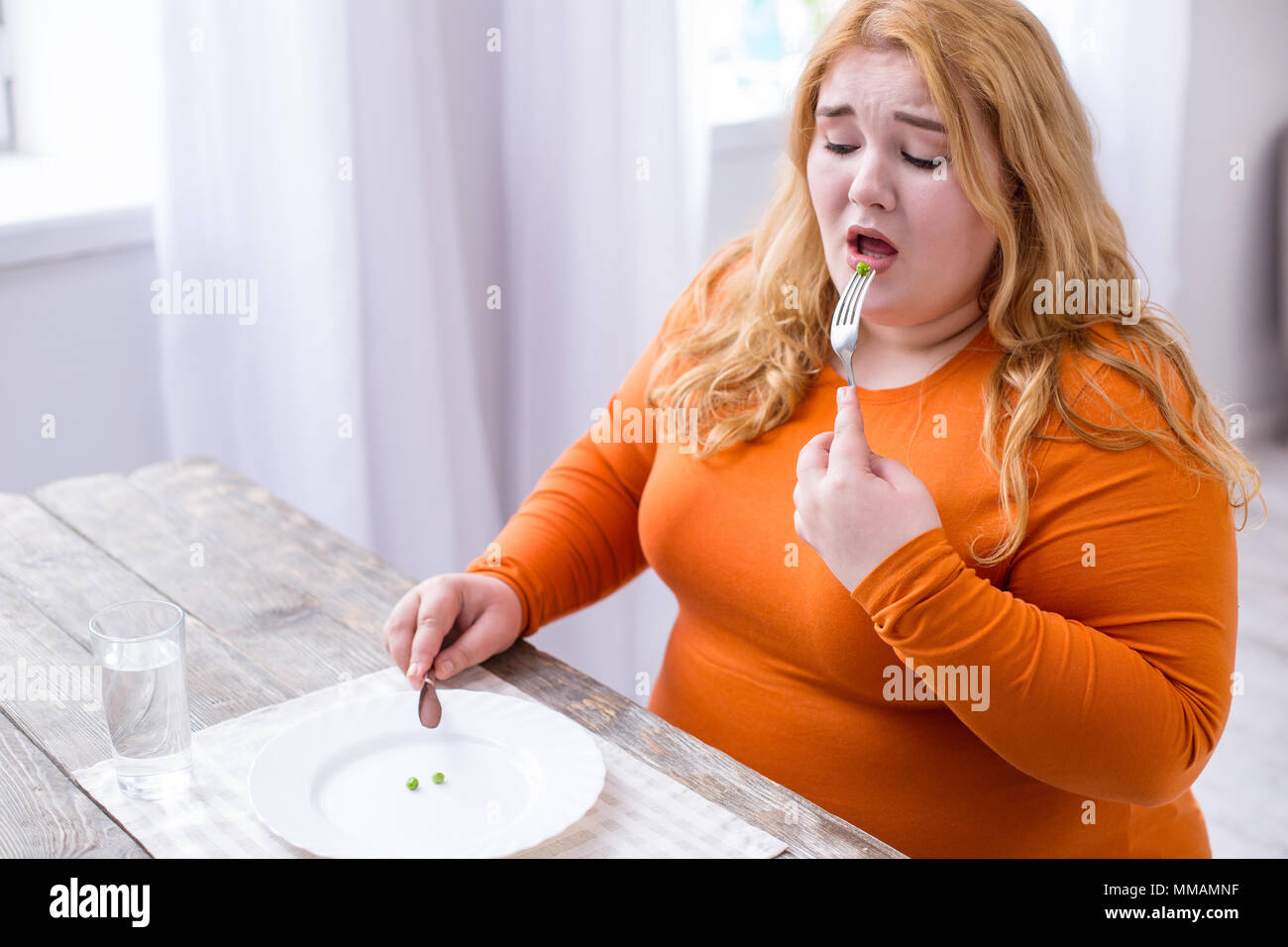 Desolate stout woman eating peas Stock Photo