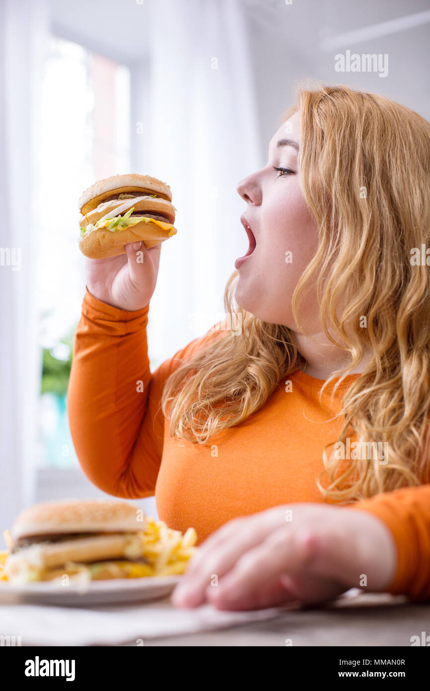 Satisfied fat woman eating fries and sandwiches Stock Photo