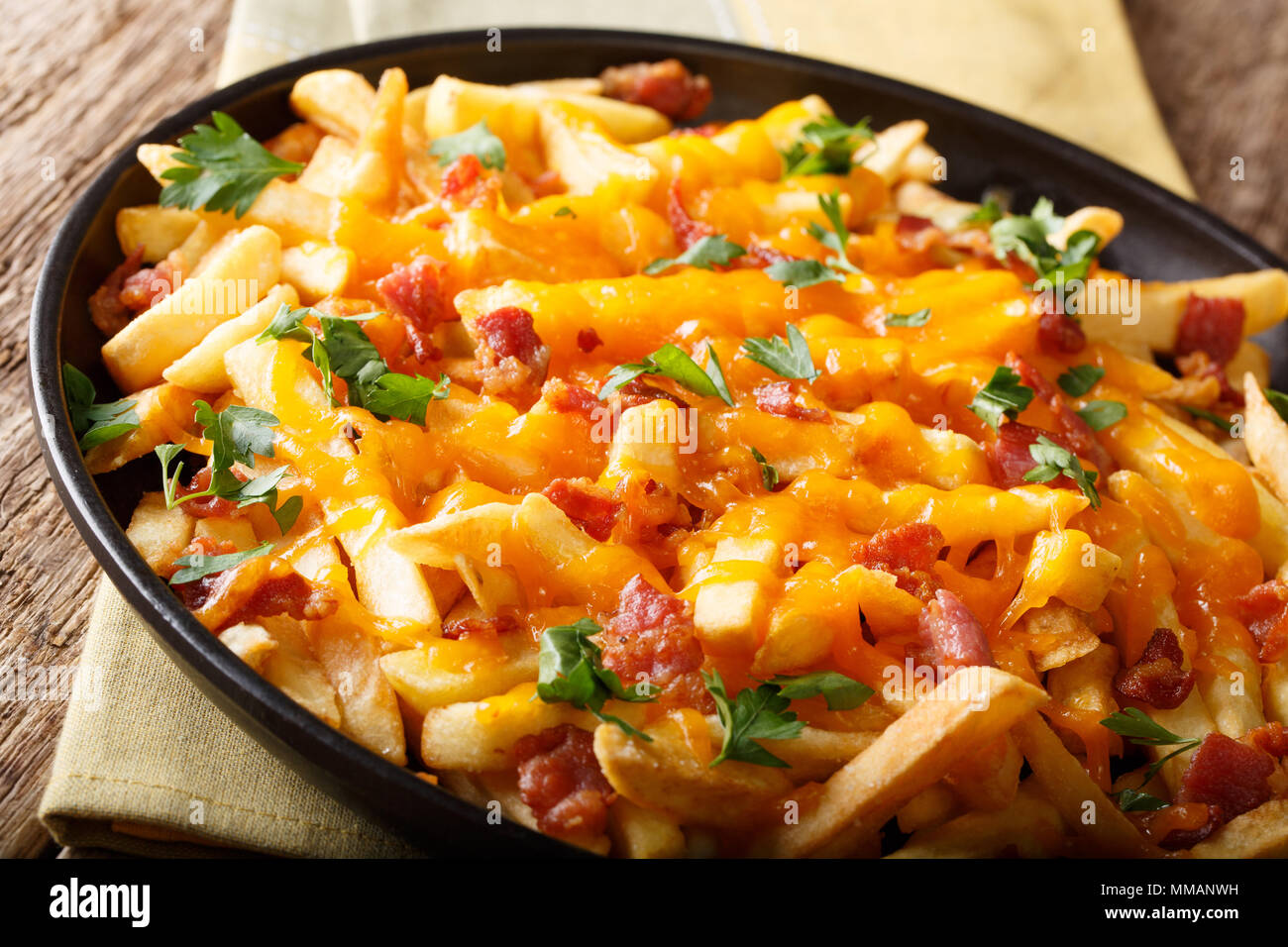 Golden fries with melted cheddar cheese, bacon and parsley closeup on a plate. horizontal Stock Photo