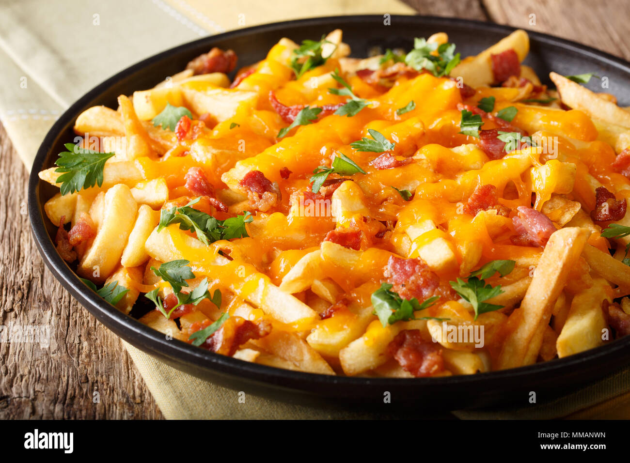 Freshly cooked French fries baked with cheddar cheese, bacon and parsley closeup on a plate. horizontal Stock Photo