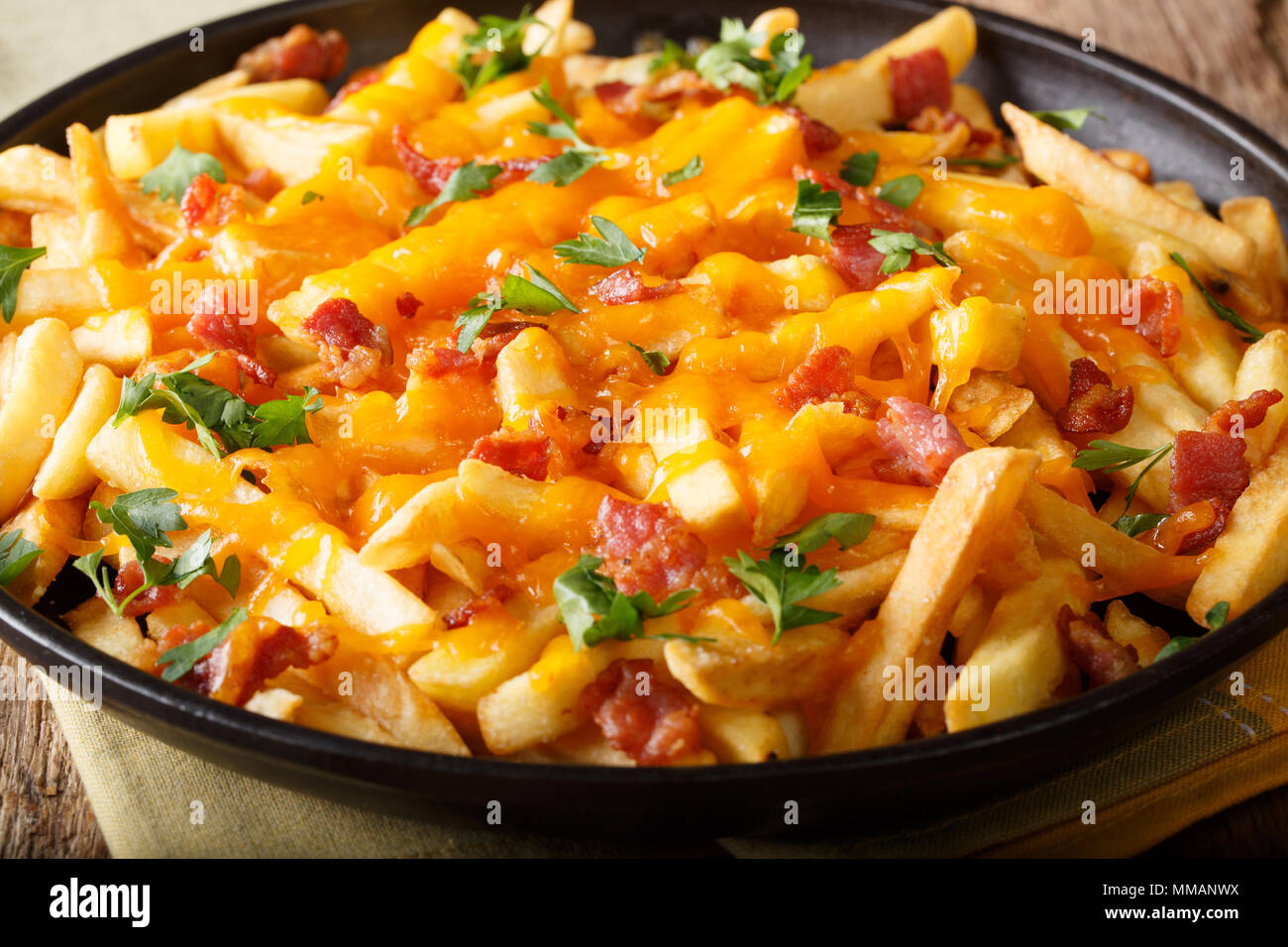 French fries baked with cheddar cheese, bacon and parsley closeup on a plate. horizontal Stock Photo