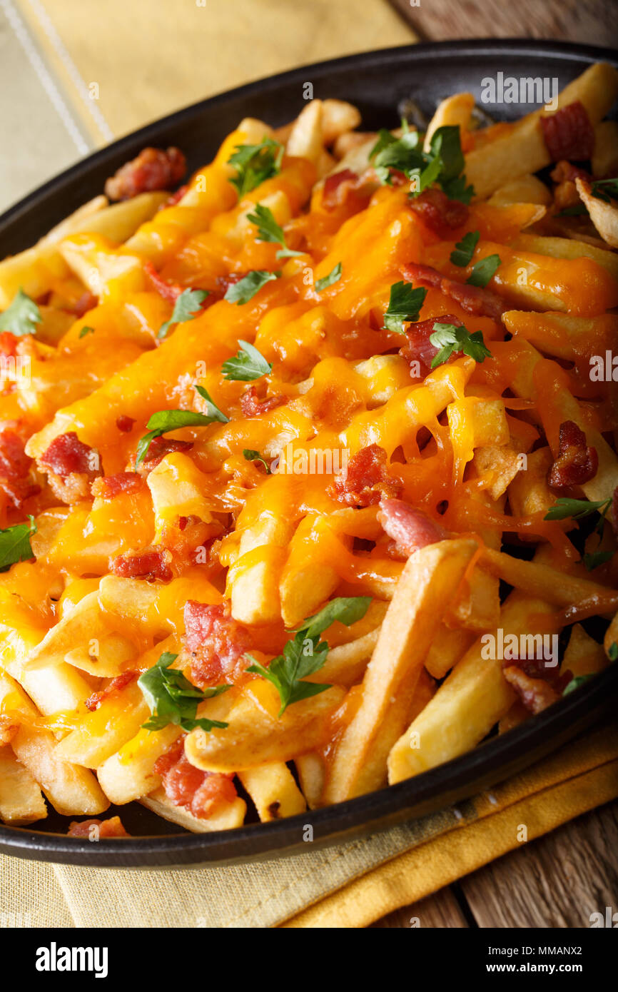 French fries with cheddar cheese, bacon and herbs close-up on a plate. vertical Stock Photo