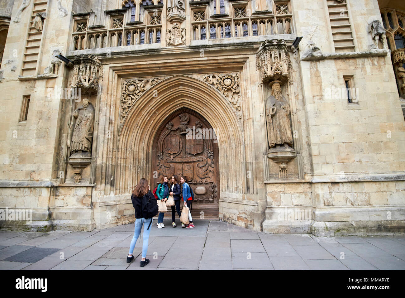 female students pose in front of large carved west front door of Bath Abbey Bath England UK ...