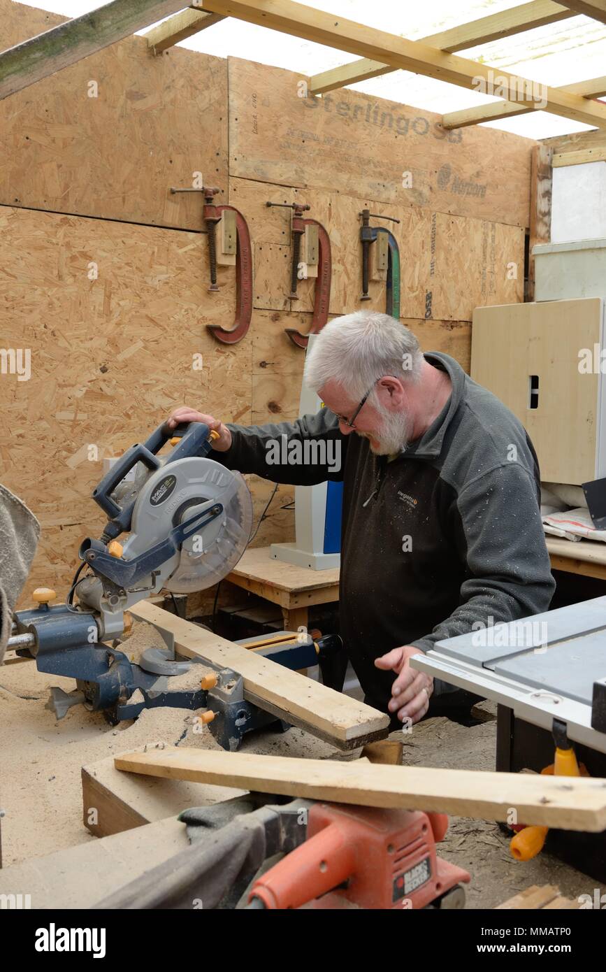 A senior retired man passes time making things from wood in his little homemade workshop in Glasgow, Scotland, UK Stock Photo