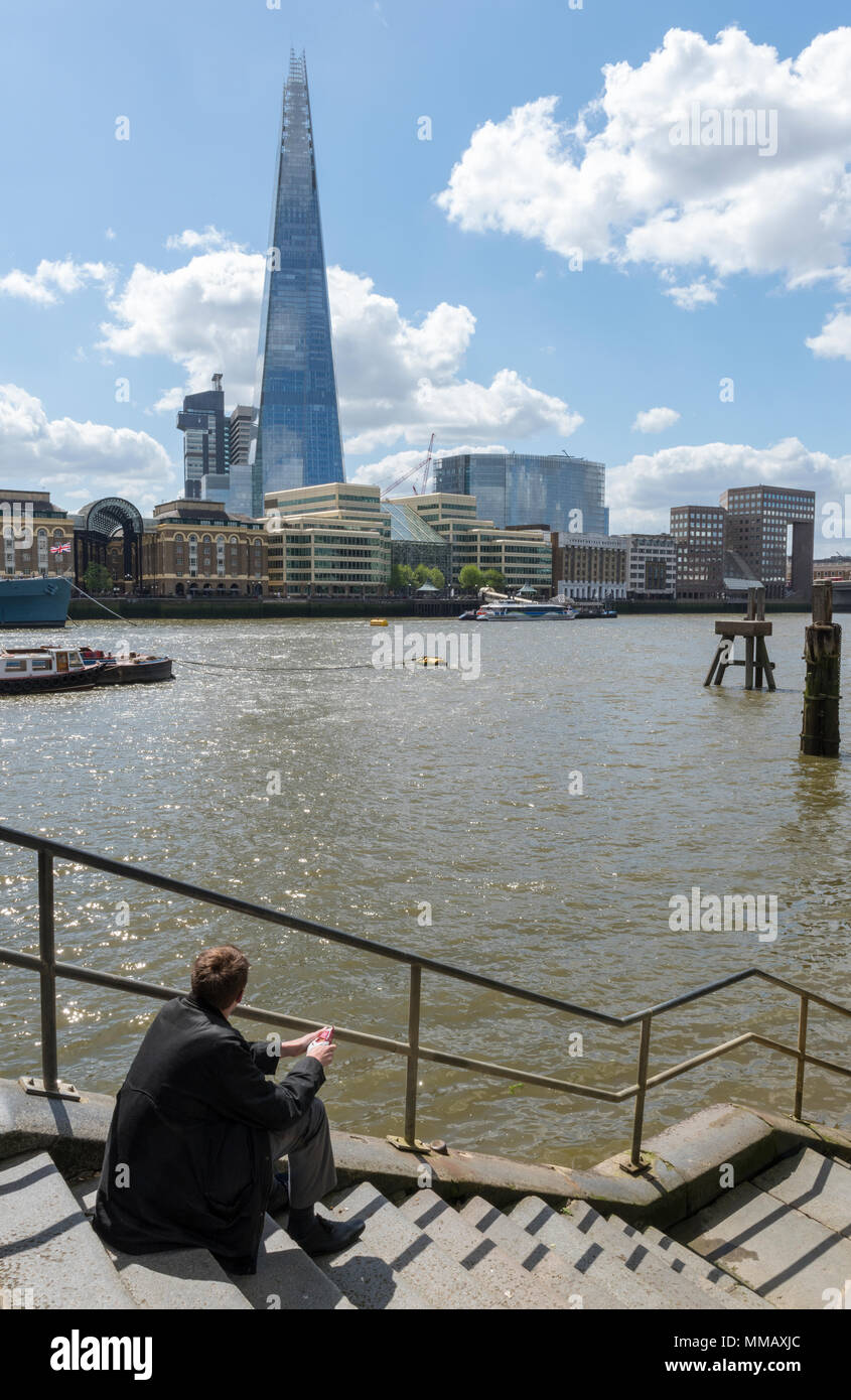 A man or businessman sitting by the side of the river thames in central london deep in thought or thinking with the shard office building across river Stock Photo