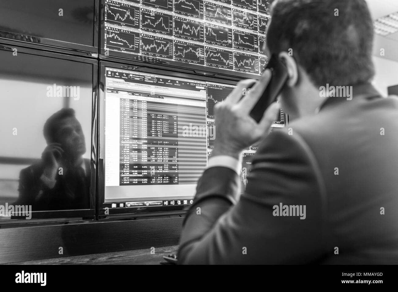 Businessman with cell phone trading stocks. Stock analyst looking at graphs, indexes and numbers on multiple computer screens. Stock trader evaluating Stock Photo