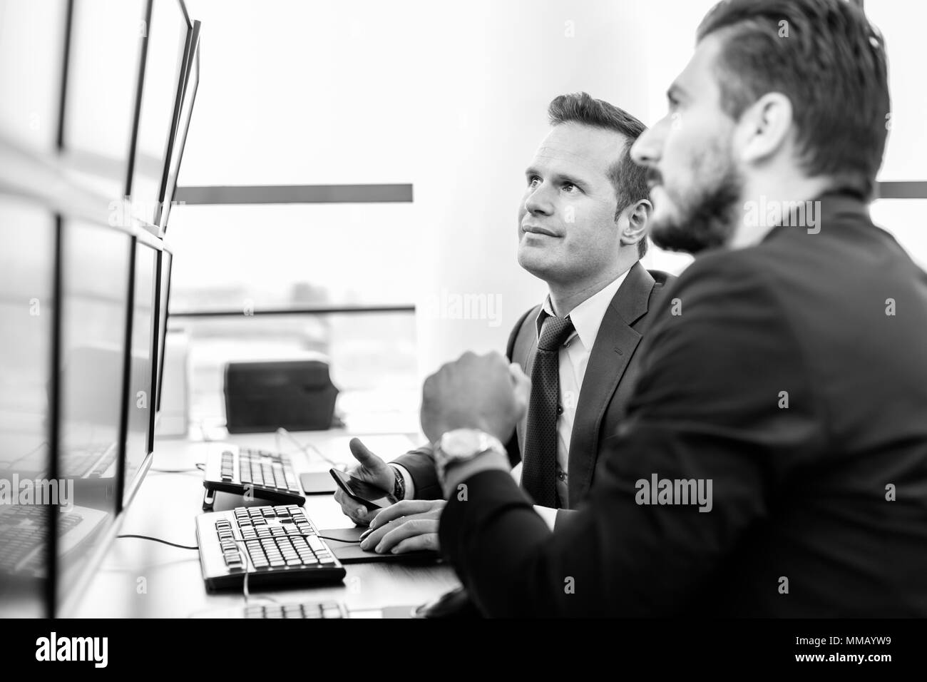 Successful businessmen trading stocks. Stock traders looking at graphs, indexes and numbers on multiple computer screens. Colleagues in traders office Stock Photo