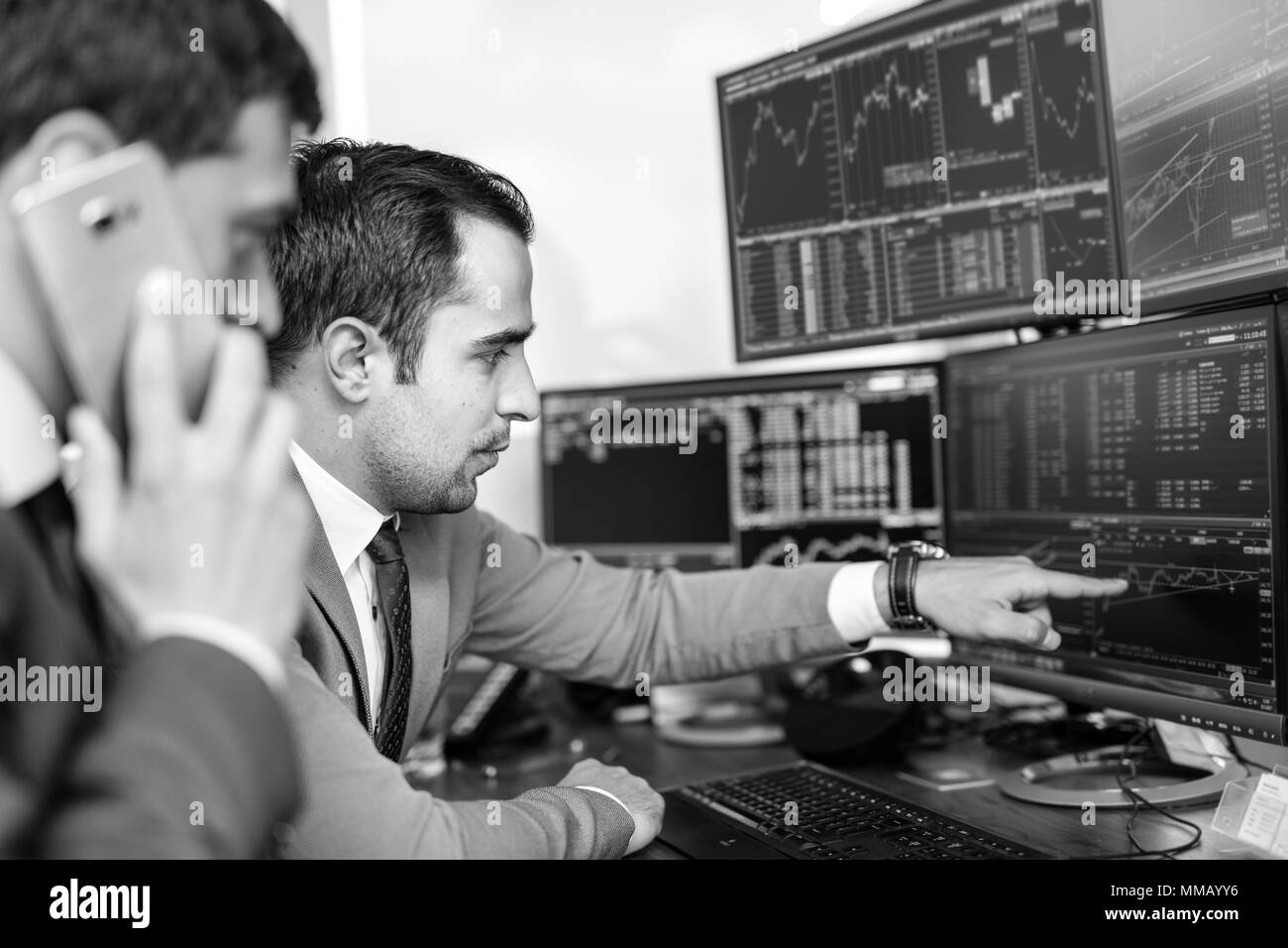 Businessmen trading stocks online. Stock brokers looking at graphs, indexes and numbers on multiple computer screens. Colleagues in discussion in trad Stock Photo
