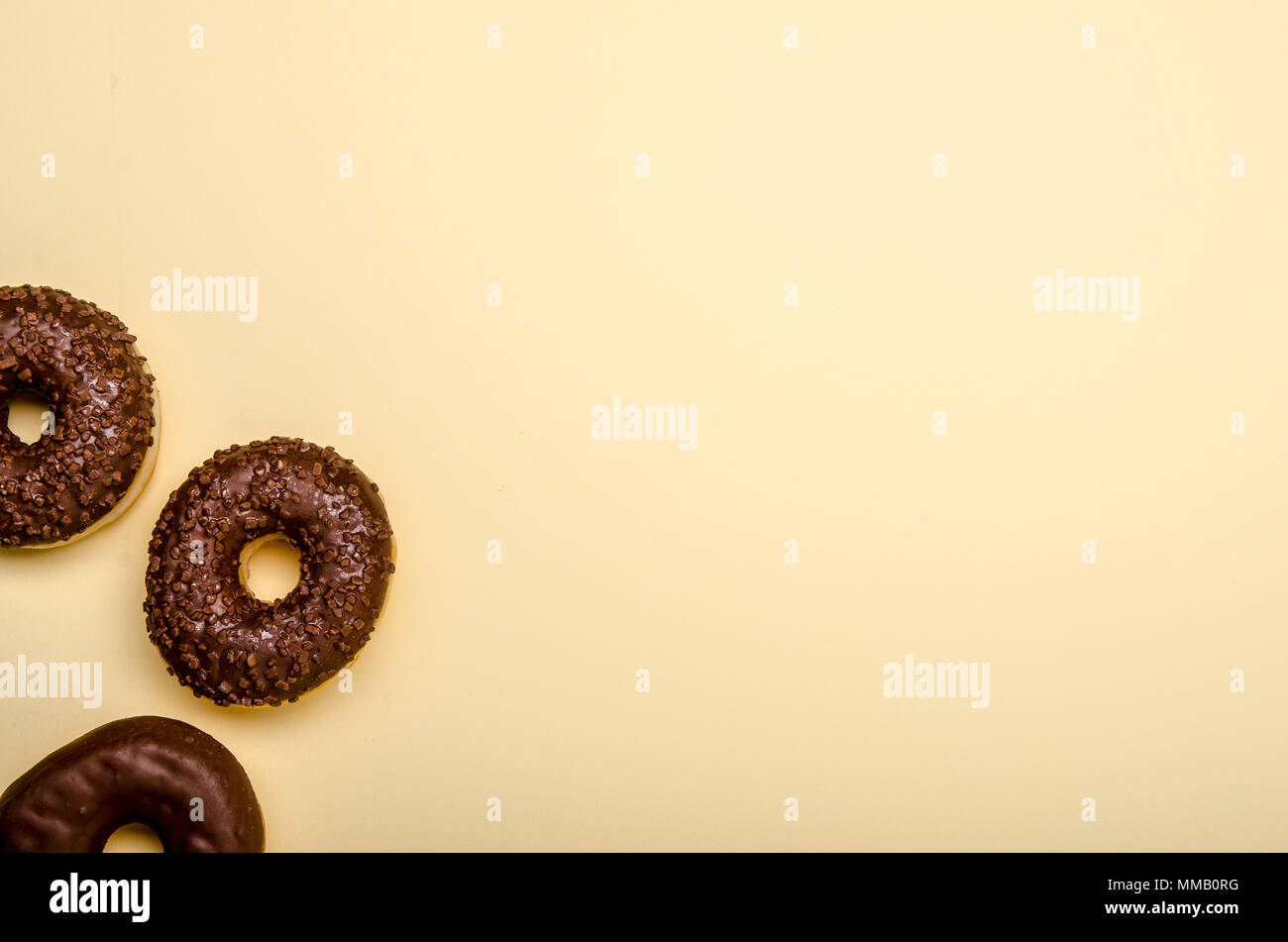 three chocolate donuts on beige background, copy space Stock Photo