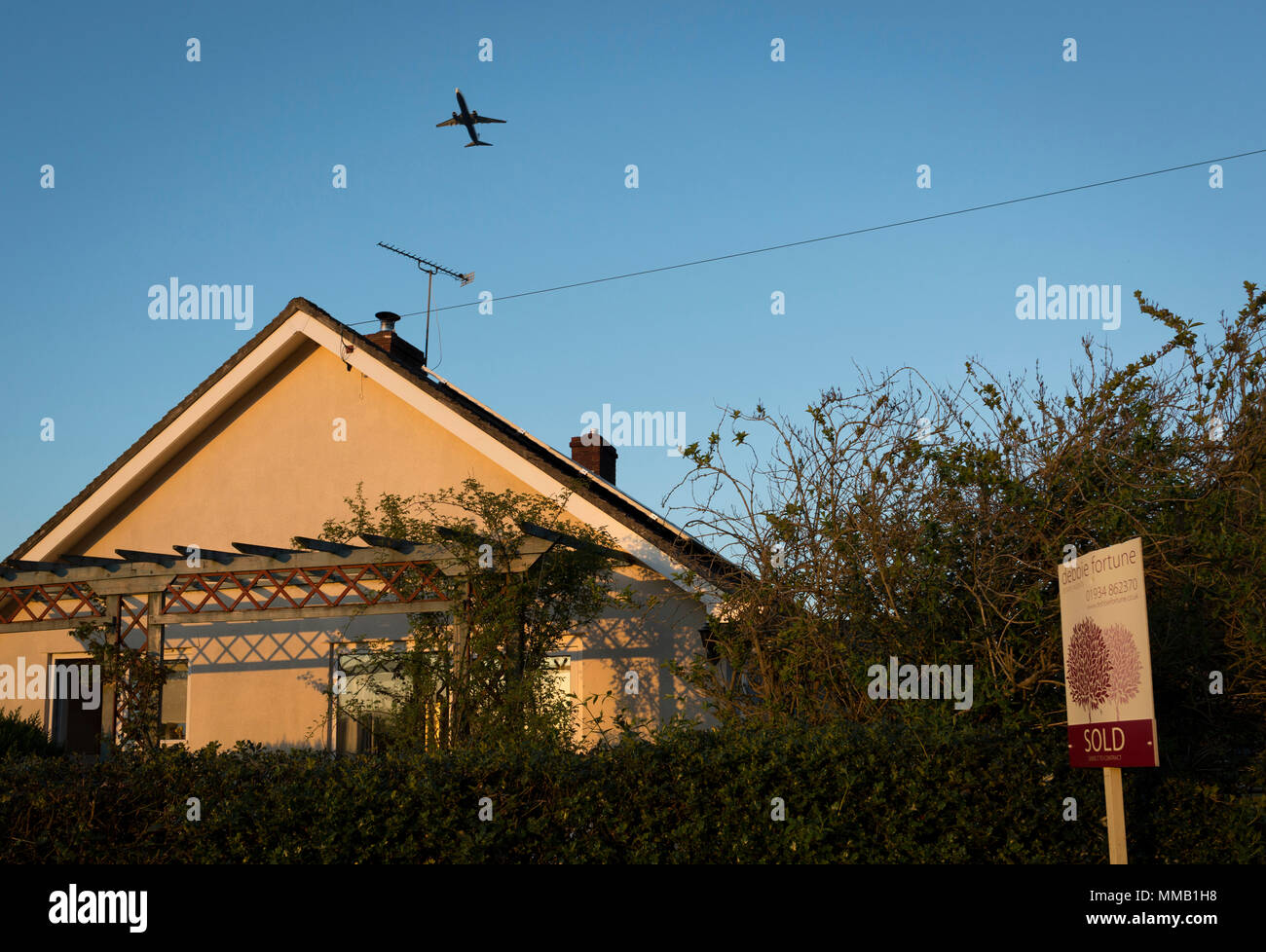 A jet airliner departing from nearby Bristol airport takes-off from a rural bungalow, recently sold by a local north Somerset estate agency, on 5th May 2018, in Wrington, North Somerset, England. Stock Photo