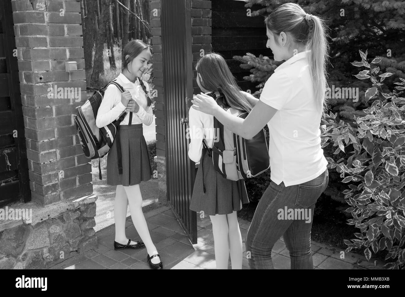 Black and white image of young mother helping daughter to put on school bags Stock Photo