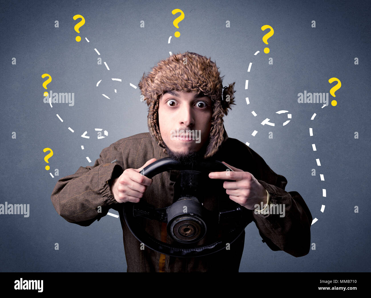 Young man holding black steering wheel with question marks around him