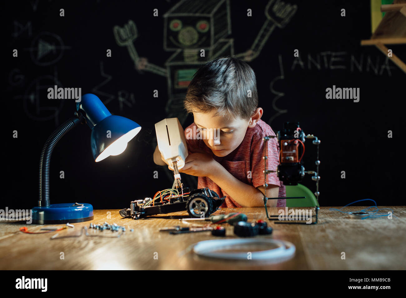 Portrait of a smart schoolboy soldering in the evening at home. Child with a soldering gun working on his school project. Stock Photo