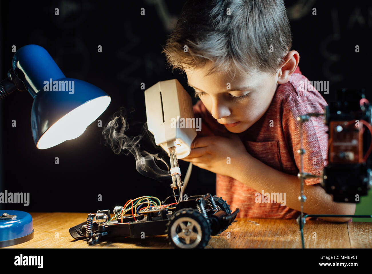 Portrait of a clever young school boy soldering metal parts of his toy car together. Focused child using a soldering gun with his school project. Stock Photo