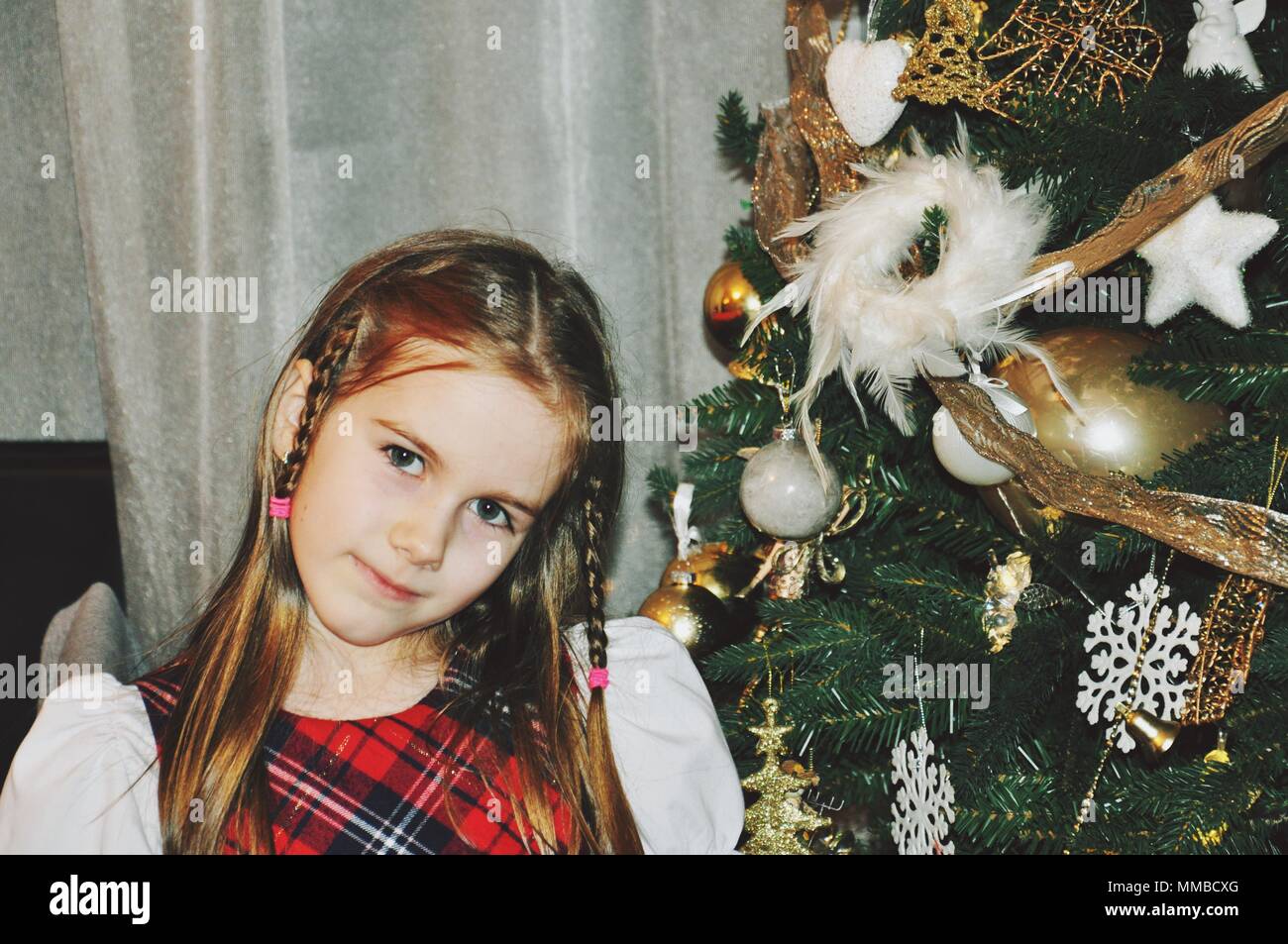 Portrait of a blonde girl child near the decorated Christmas tree, front view Stock Photo