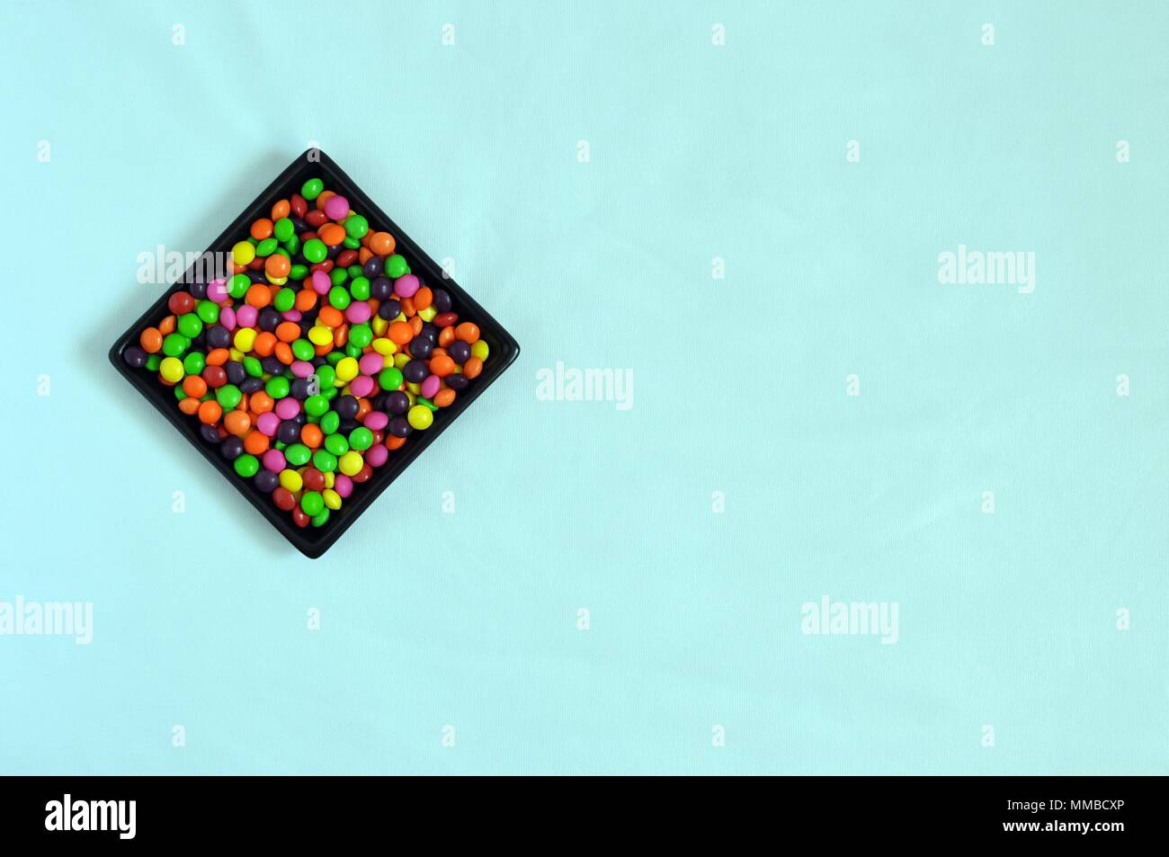 Black plate filled with litlle colorful candies on light blue backgroung, copy space, top view Stock Photo
