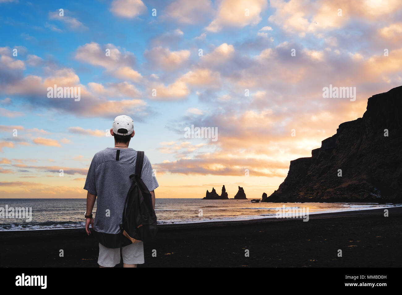a man with backpack standing on black sand beach in sunset, Iceland. Vacation travelling in summer and summer recreation pursuit concept Stock Photo