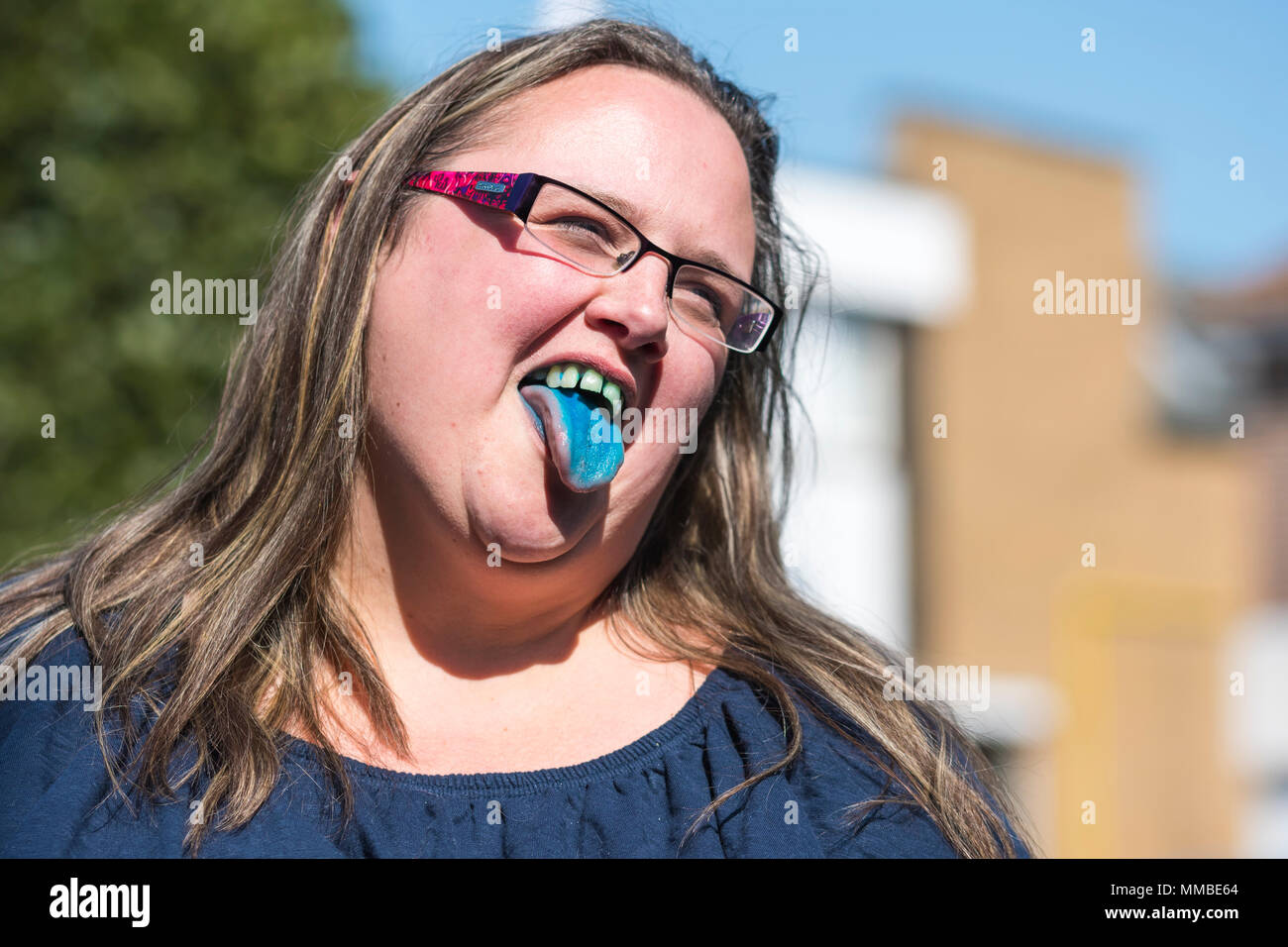 Woman sticking tongue out after drinking blue slush puppy drink, showing blue stains on her tongue and teeth, while smiling in Summer. Happy concept. Stock Photo