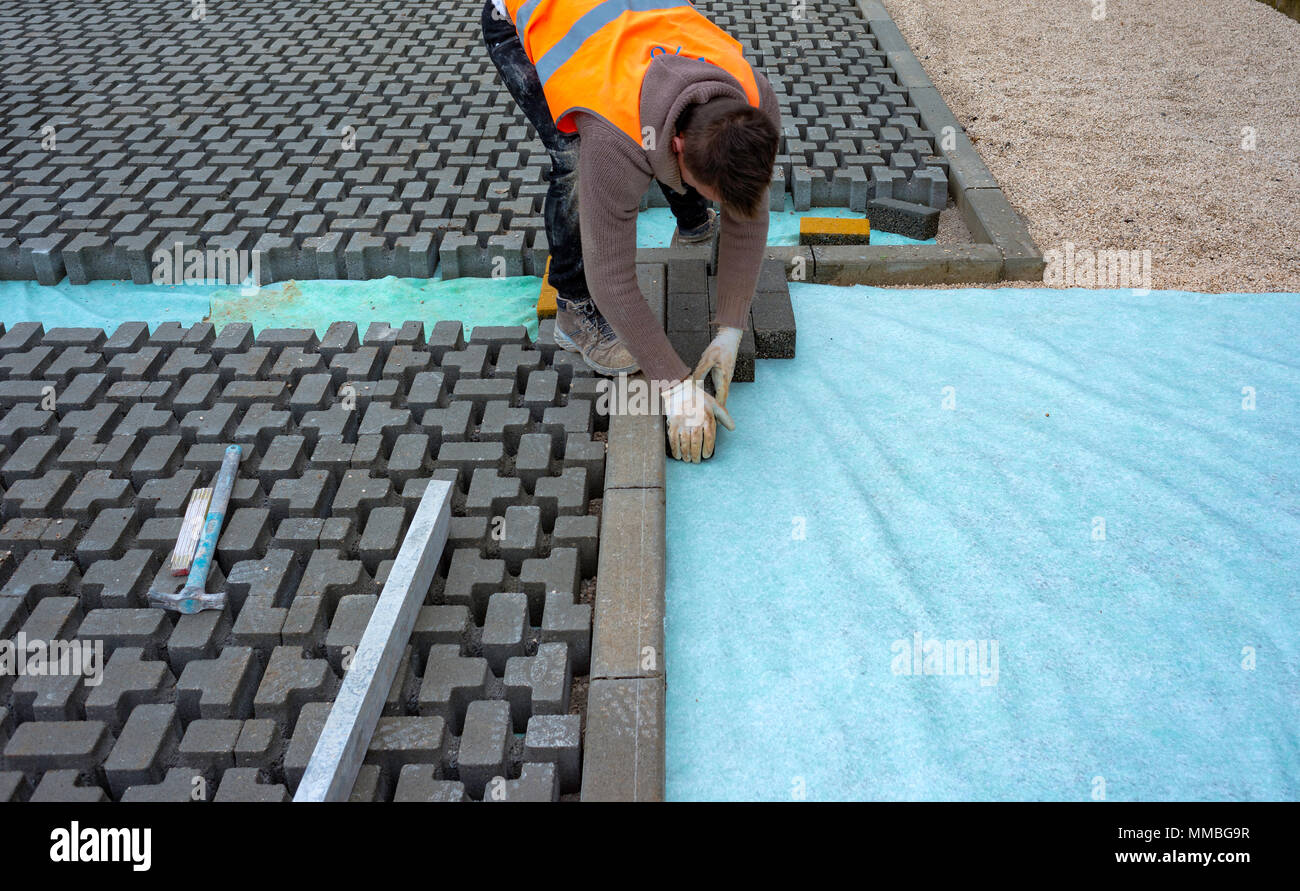 Construction worker laying interlocking paving concrete onto sheet nonwoven bedding sand and fitting them into place. Stock Photo