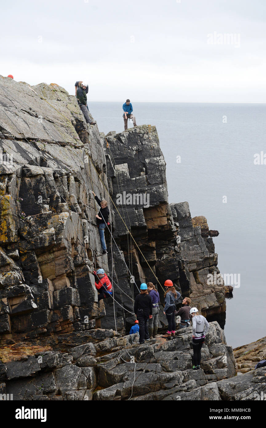 Climbers club climbing and abseiling on cliffs next to the sea. A variety of young and old participants Stock Photo