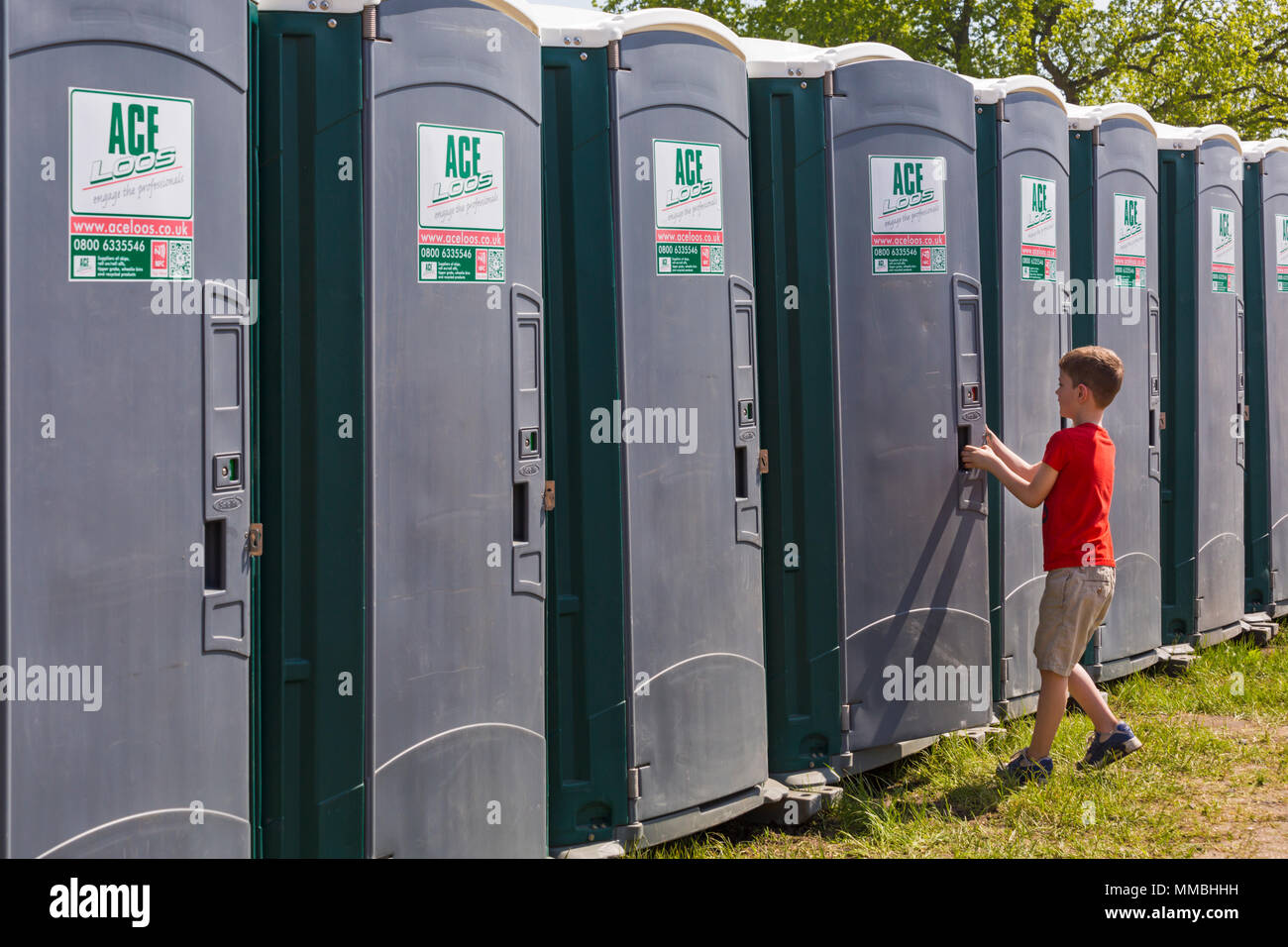 Row of portable toilets with boy opening door to enter one at Hampshire Game & Country Fair, Netley Marsh, Hampshire UK in May Stock Photo