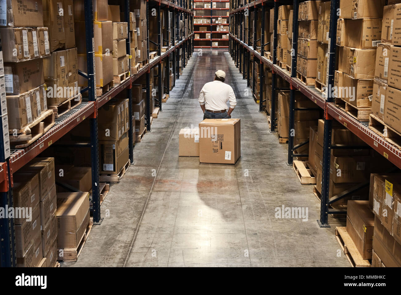 Single warehouse worker in between large racks of cardboard boxes on
