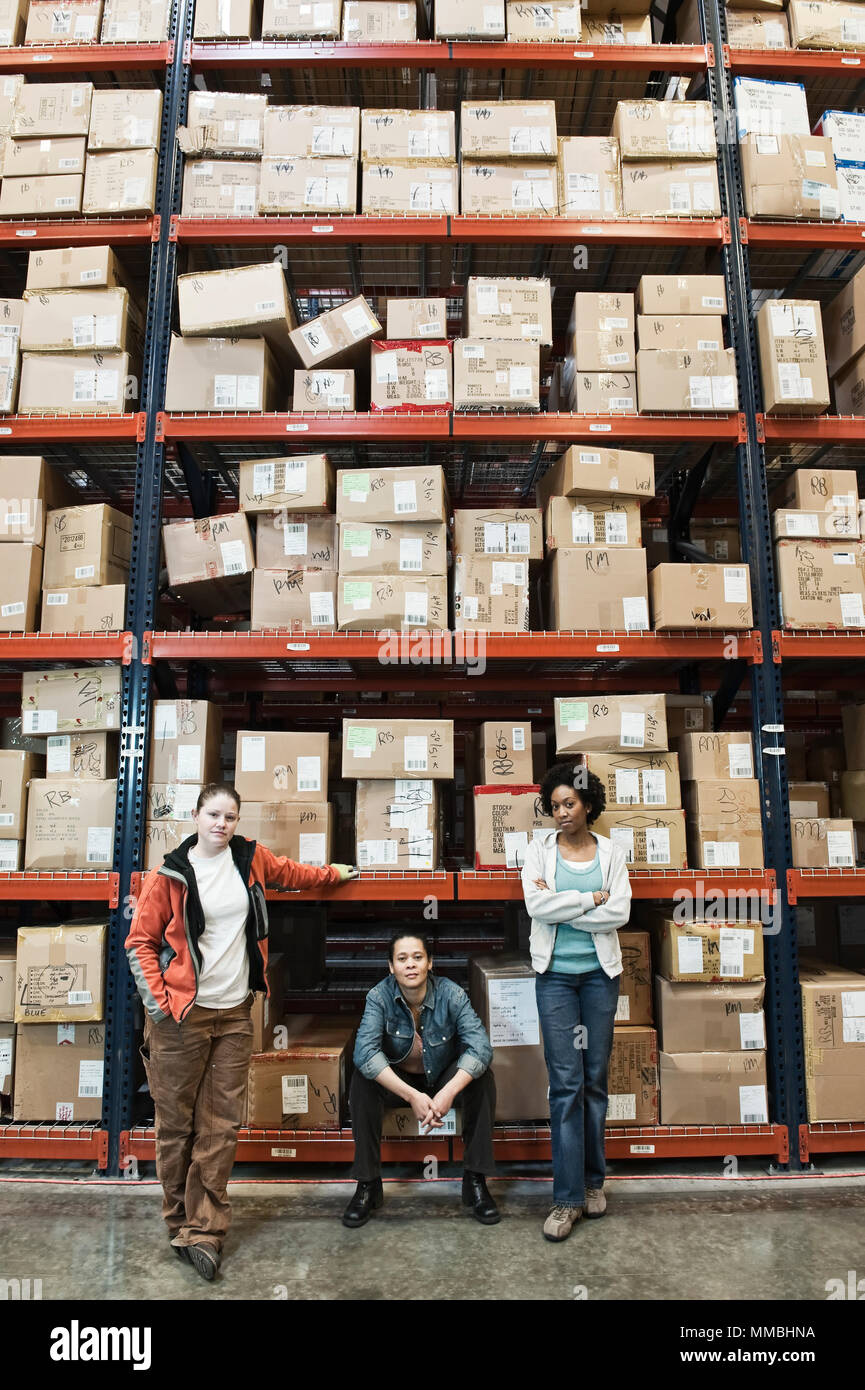 Team portrait of multi-ethnic female warehouse workers in a large distrubiton warehouse full of products stored on pallets in cardboard boxes on large Stock Photo