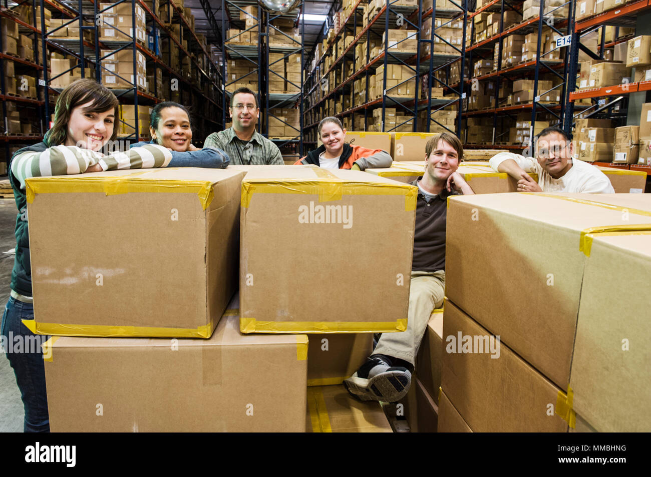Team portrait of multi-ethnic male and female warehouse workers in a large distrubiton warehouse full of products stored on pallets in cardboard boxes Stock Photo