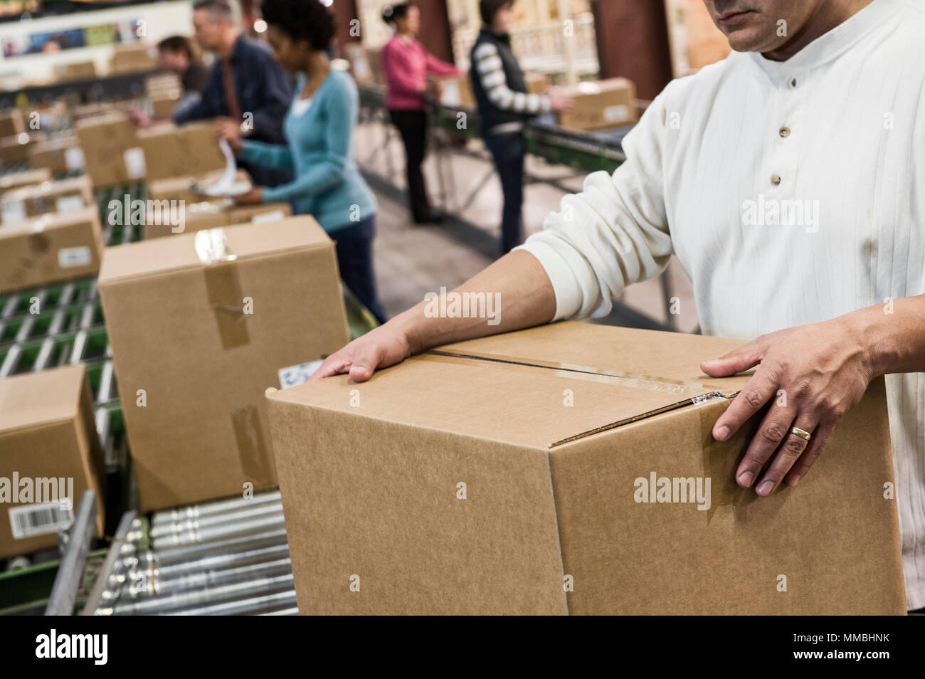 Team of multi-ethnic warehouse workers working on a motorized feed conveyor in a large distribution warehouse of products stored in  carboard boxes. Stock Photo