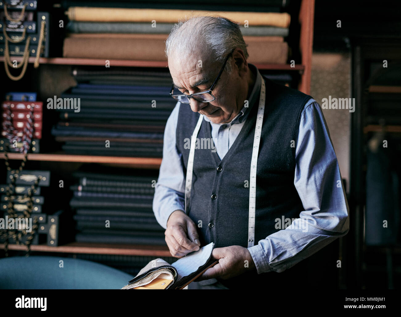 Tailor with measuring tape around his neck inspecting fabric samples. Stock Photo