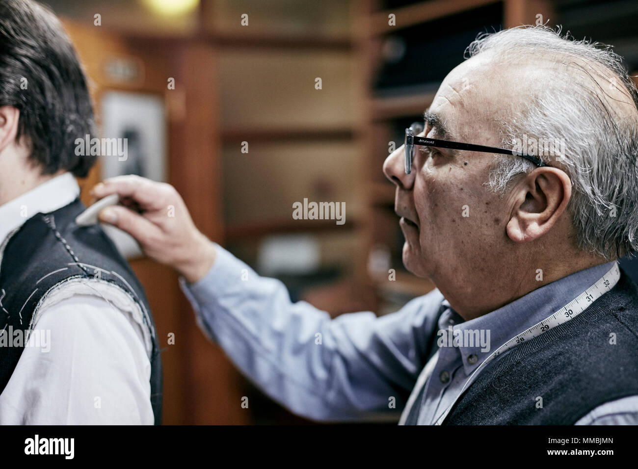 Tailor fitting a jacket on a customer using tailor's chalk to mark the fabric  mature man grey hair glasses client bespoke tailoring Stock Photo