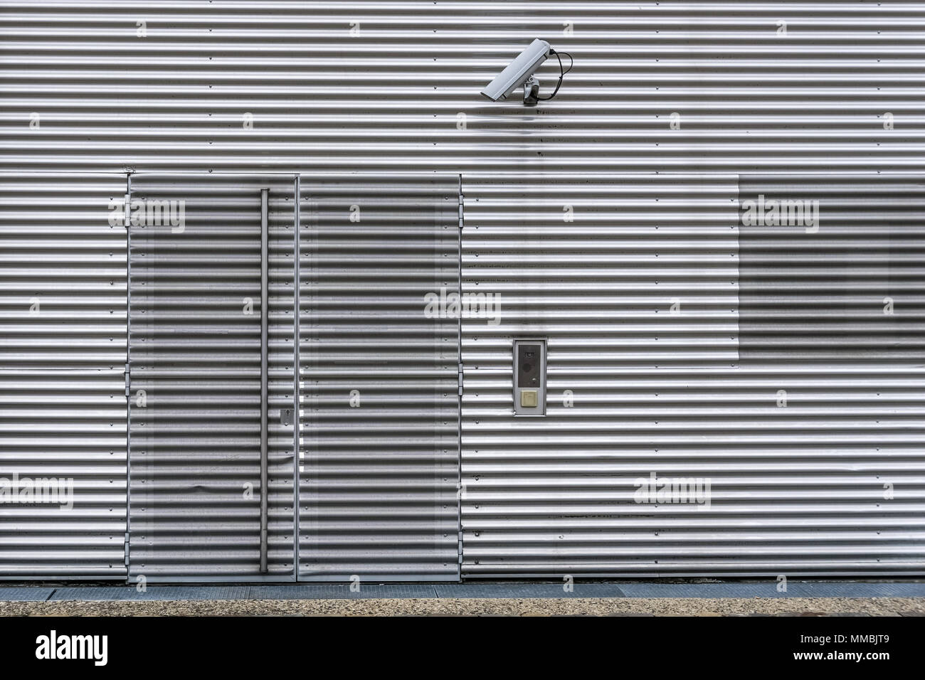 Exterior video surveillance and security system with CCTV camera on a corrugated iron wall to watch over the entrance of the building. Stock Photo