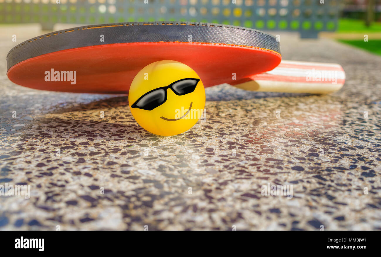 Tennis table paddle with a smiley ball below it on a stone tennis table in a park. Loving sport concept. Stock Photo