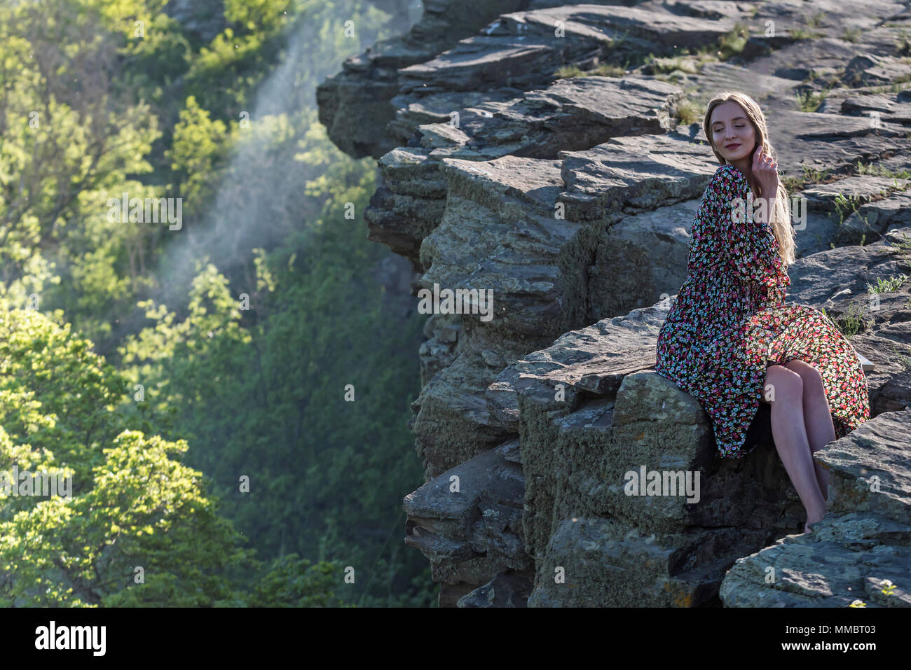 Beautiful girl in dress sits on rock in nature Stock Photo - Alamy