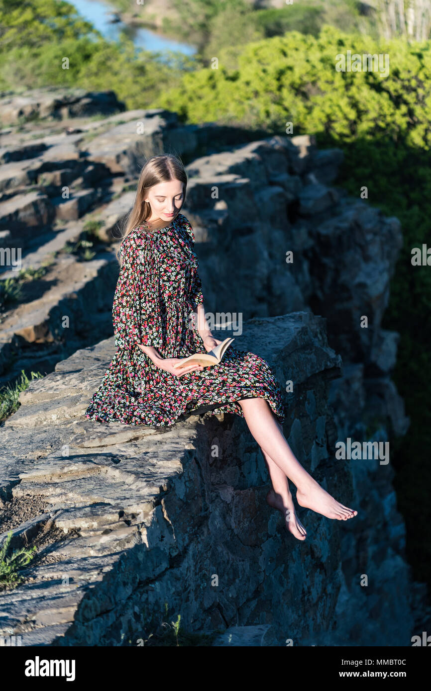 Beautiful girl in dress sits on rock in nature Stock Photo - Alamy