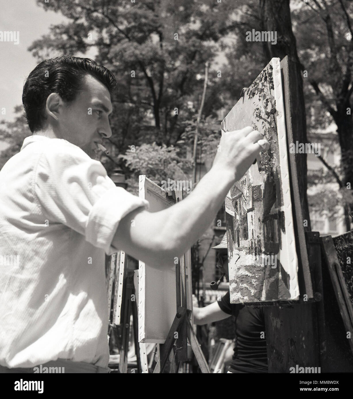 1950s, historical picture, a male street artist painting on a canvas outside, at the Place du Tertre, a square at Montmartre in Paris, France, famous for its artists and artistic history. Stock Photo