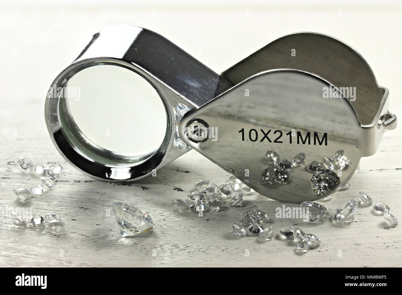 brilliant cut diamonds with folding magnifier on wooden background Stock Photo