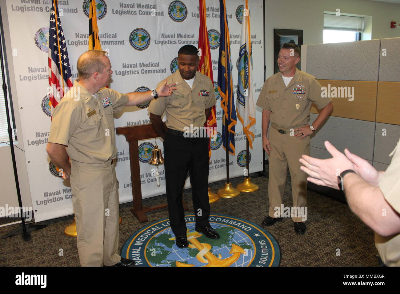 Capt. Tim Richardson, Naval Medical Logistics Command’s commanding officer, notices that LS2 Jossani Josiah is out of uniform during an unscheduled ceremony. Moments later, Josiah was meritoriously promoted to Petty Officer 1st Class. Command Master Chief Patrick West participates in the announcement. Stock Photo