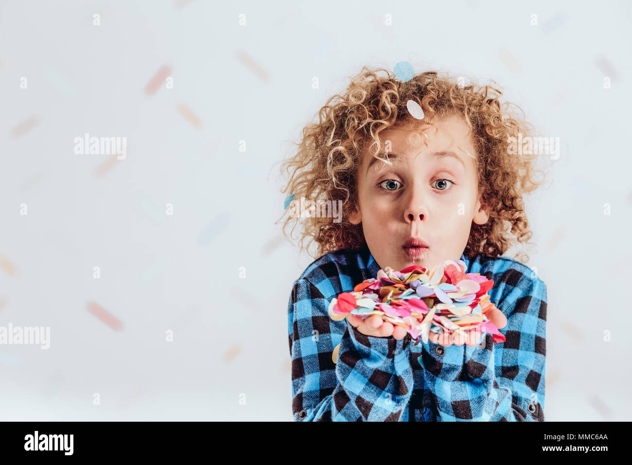 Young blond boy holding confetti in his hands and blowing at it Stock Photo