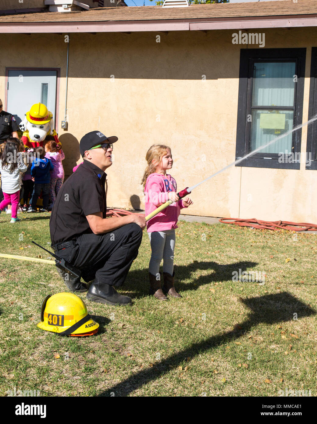 Paul Aguilar, fire prevention officer with Fire and Emergency Services, demonstrates fire hose operations, while Sparky meets children from the Child Development Center during a fire safety tour on Marine Corps Logistics Base Barstow, Calif., Oct. 10. Stock Photo