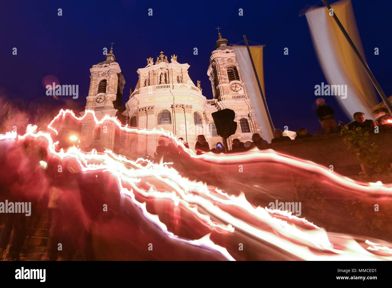 10 May 2018, Germany, Weingarten: Numerous people walk pass the basilica during a candlelight procession. Only light strips can be seen due to the bulb exposure during the blue hour. A day before the Blutritt, people ride to the hill in Weingarten during the largest riding procession in Europe. Photo: Felix Kästle/dpa Stock Photo